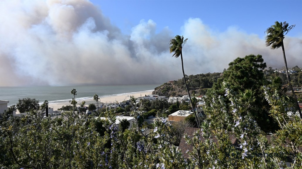 Fumée de l'incendie de Palisades visible au-dessus de l'océan. Vue depuis Santa Monica incluant des arbres verts, d'autres plantes et des bâtiments près de la côte.