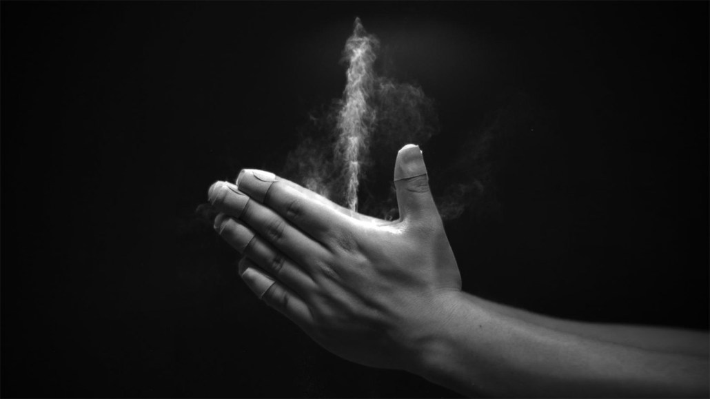 Photographie en noir et blanc de deux mains applaudissant, expulsant un jet blanc de poudre pour bébé entre le pouce et l'index