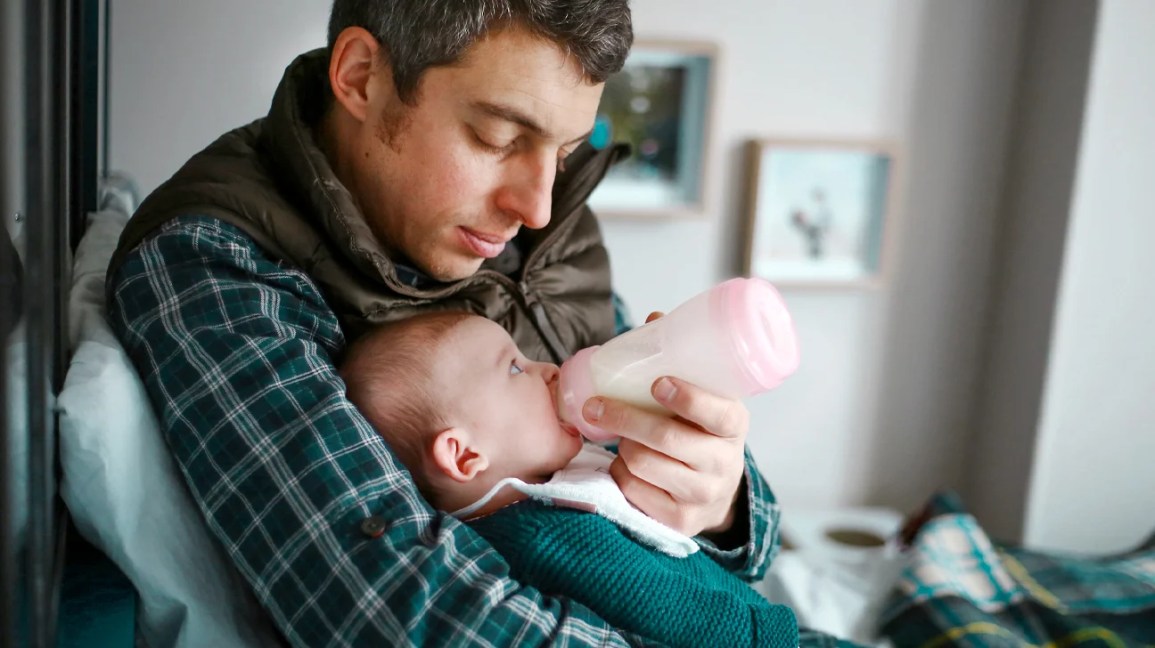 Un père nourrissant son bébé au biberon dans une position adaptée