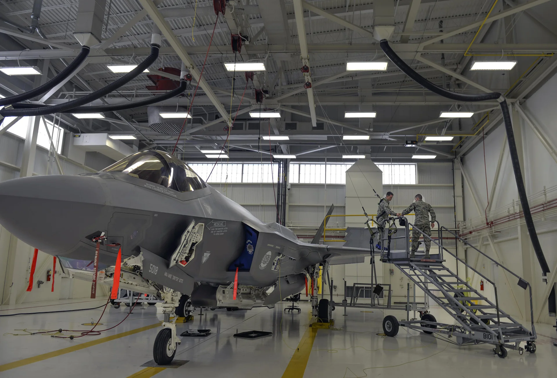 Techniciens de maintenance travaillant sur un moteur d'avion de chasse en hangar.