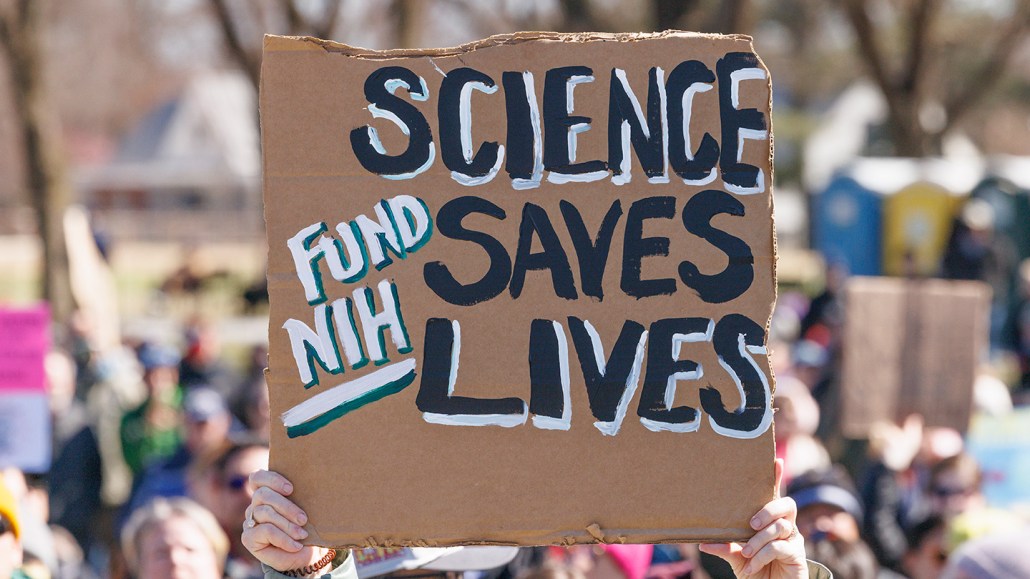 Un manifestant tient une pancarte indiquant Science Saves Lives au milieu d'une foule