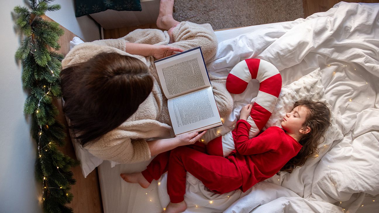 Un parent lit un livre à son enfant dans un lit, créant un moment de calme avant le sommeil avec une peluche géante.