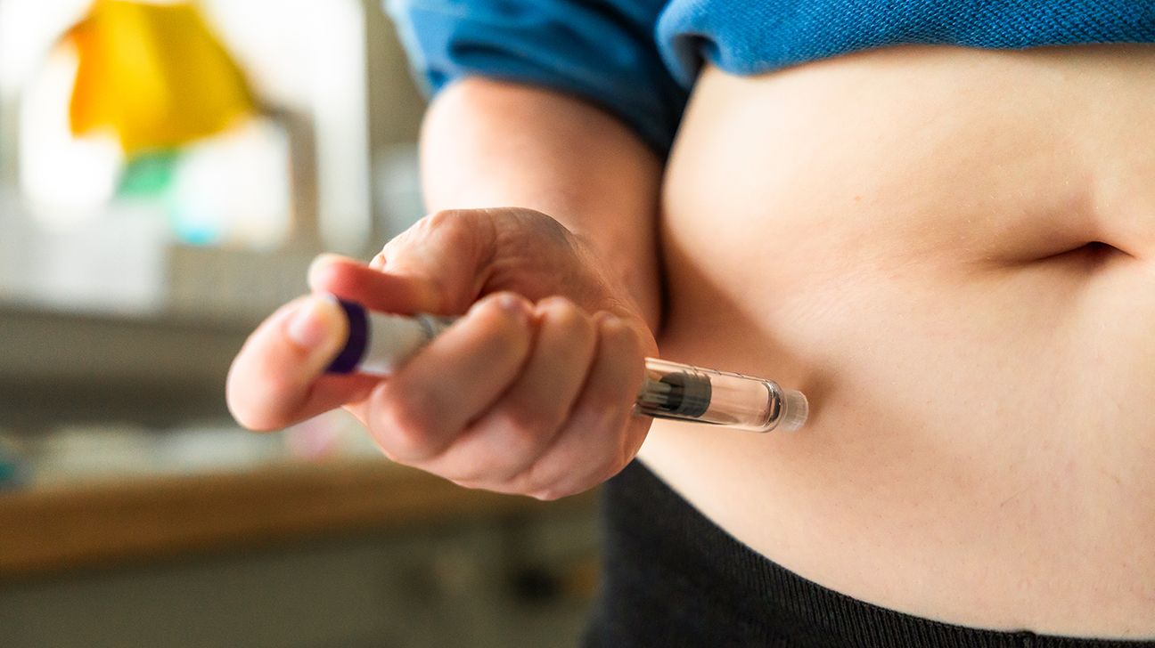 Plan rapproché d'une patiente s'administrant une injection sous-cutanée au niveau de l'abdomen à l'aide d'un stylo prérempli