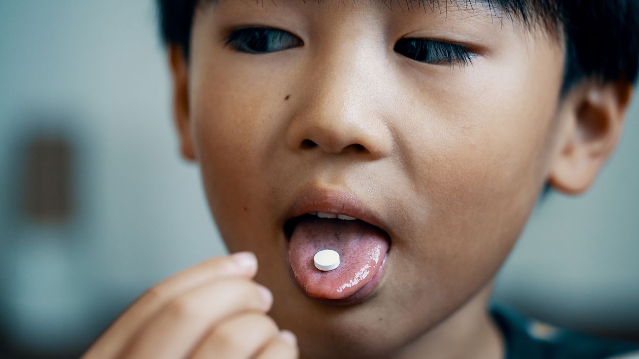 Jeune garçon avec un comprimé posé sur la langue, illustrant la difficulté de la déglutition médicamenteuse chez l'enfant.
