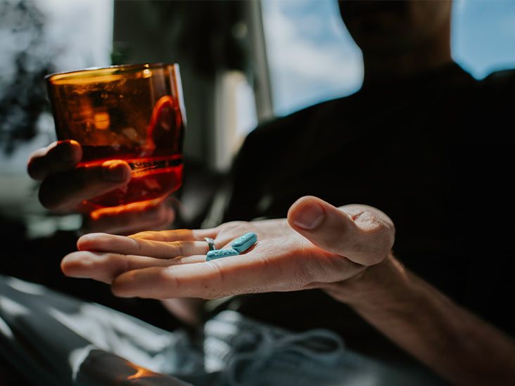 Une personne tient des pilules dans une main et un verre d'eau dans l'autre