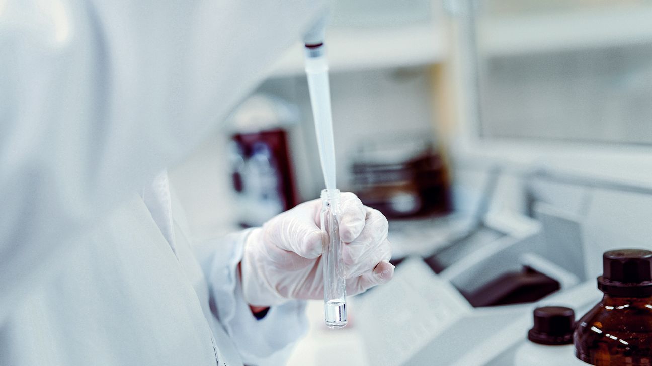 Un chercheur manipulant des flacons dans un laboratoire stérile, illustrant le développement de traitements pharmacologiques.