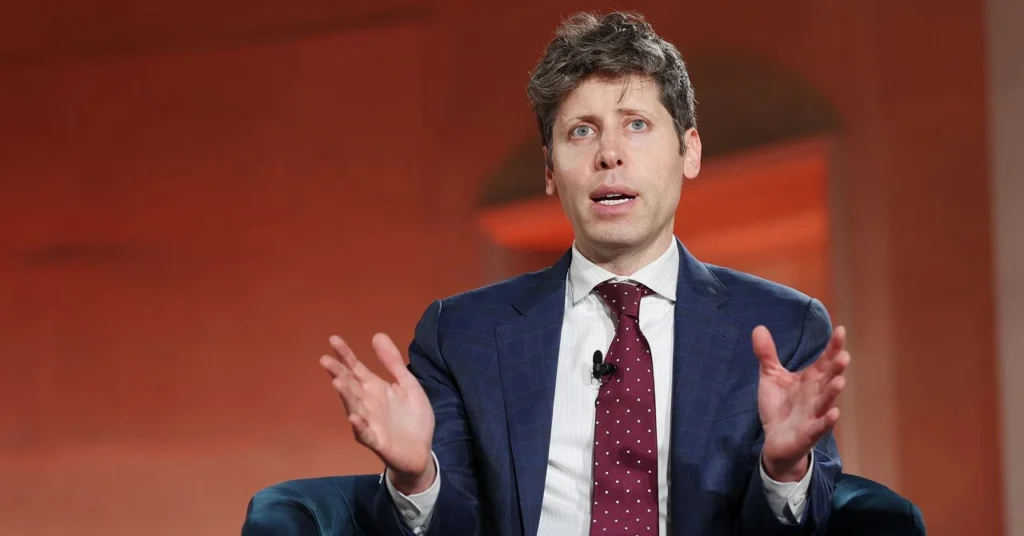 Sam Altman assis, en costume bleu et cravate bordeaux, les mains levées devant un fond orangé.